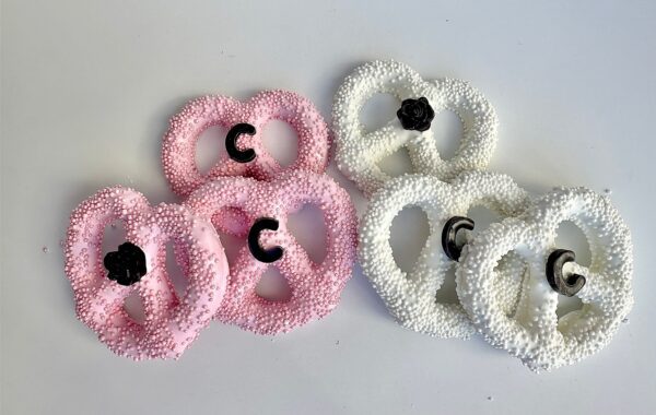 Pink and white textured pretzel shapes, adorned with black rose embellishments, are artistically arranged alongside 12-Designer LOGO Purses suitable for a birthday party, wedding, baby shower, or purse party favors on a white surface.