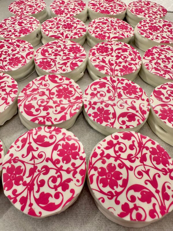 A 12-pack of Chocolate-Covered Oreos with intricate pink floral scroll patterns on white icing, perfect for weddings, birthdays, parties, or baby showers.