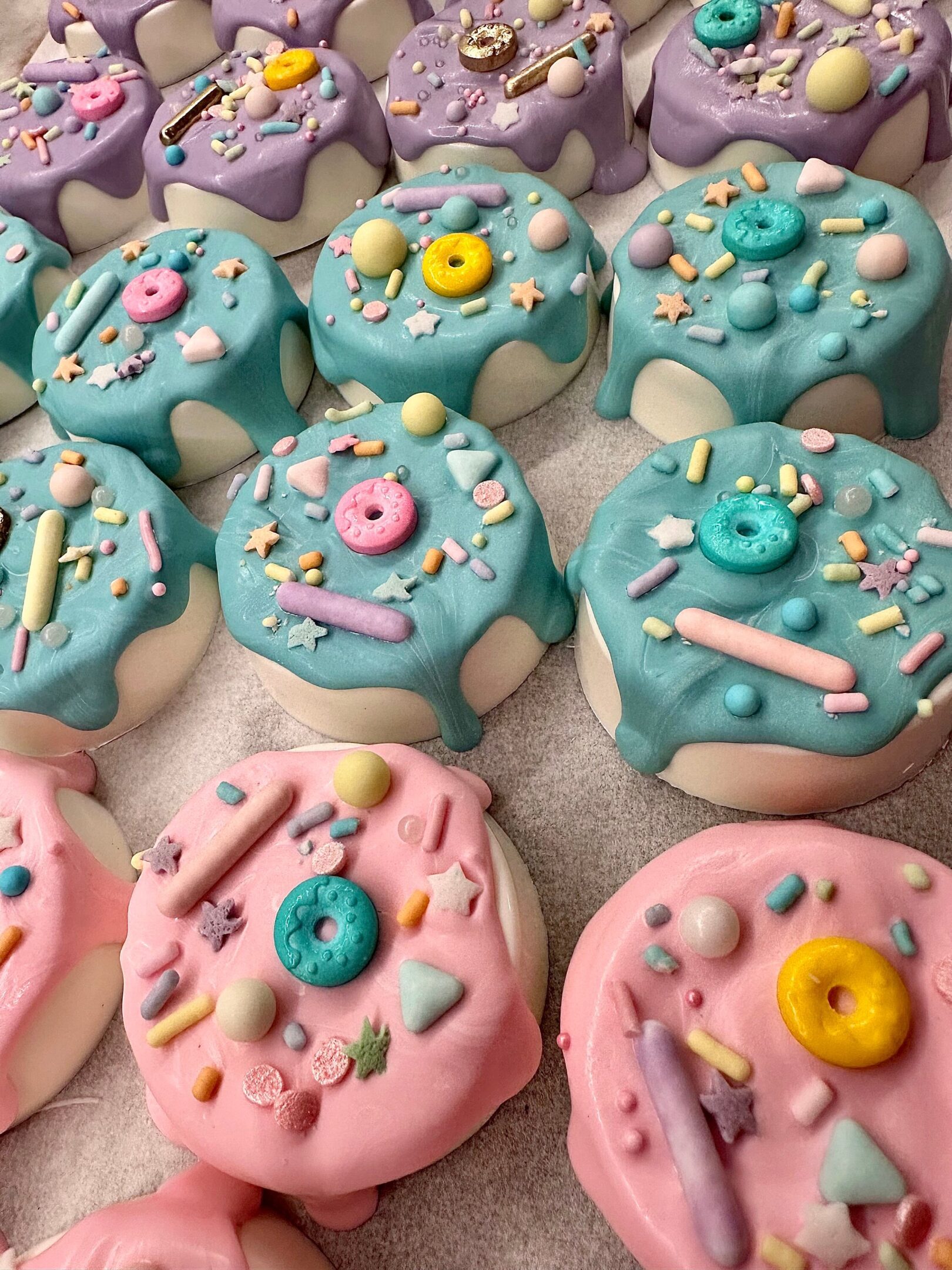 Vibrant treats featuring chocolate-covered Oreos in pastel pink, blue, and purple icing, adorned with assorted decorative candies.