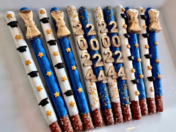 Blue and white iced pretzel rods, decorated with silver and gold stars, graduation caps, bells, and numbers 222, 000, 2222, 4444. Product: 12-Graduation 2024 Gold Diploma Chocolate Covered Pretzel Rods For Graduation Party/Graduation Favors.