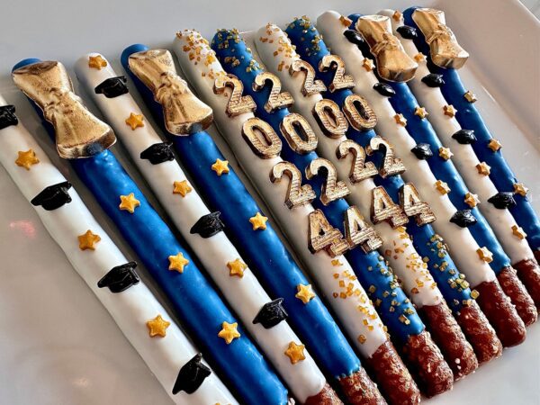 Chocolate-covered pretzel rods decorated in blue, white, and gold with "222," "0000," "4444" numbers, golden stars, and graduation cap motifs. Product: 12-Graduation 2024 Gold Diploma Chocolate Covered Pretzel Rods for Graduation Party/Graduation Favors.