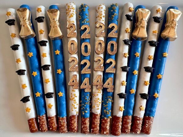 Graduation-themed pretzel sticks in blue and white, adorned with gold stars, black hats, and gold glitter numbers from the 12-Graduation 2024 Gold Diploma Chocolate Covered Pretzel Rods for Graduation Party/Graduation Favors set.