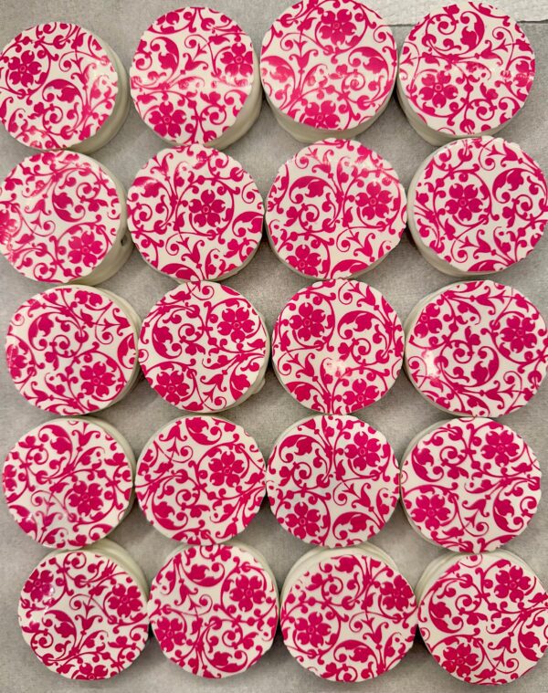 Twenty 12-Pink Floral Scroll Chocolate Covered Oreos from the gift box set are arranged in a grid on a gray surface.