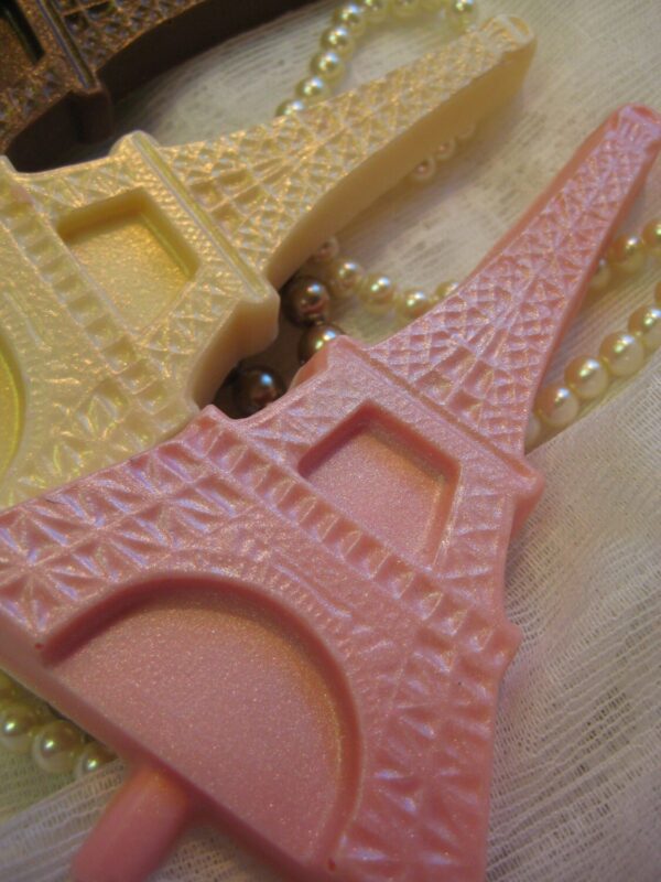 Eiffel Tower-shaped chocolate lollipop favors in pink, white, and yellow, featuring textured details, arranged on lace fabric adorned with pearls.
