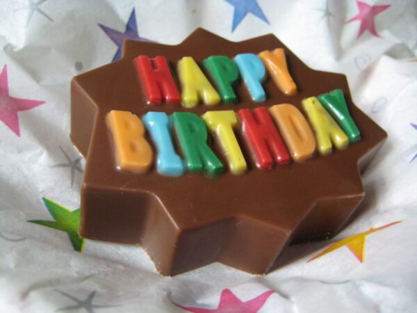 Star-shaped chocolate-covered Oreo with colorful "Happy Birthday" letters on a starry background.