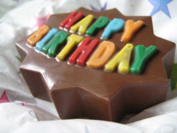 The "12-Happy Birthday Chocolate Covered Oreo Party Favors" feature star-shaped chocolate with vibrant letters spelling "HAPPY BIRTHDAY," set against patterned fabric.