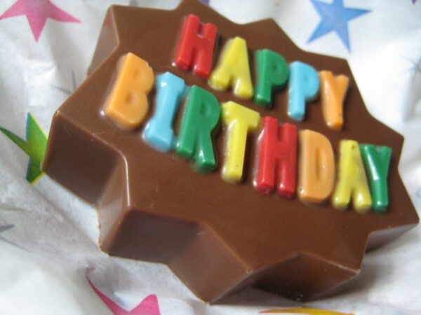 A 12-pack of Happy Birthday Chocolate Covered Oreos with colorful letters sits on star-patterned wrapping paper.