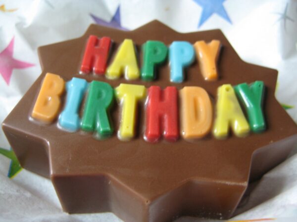 A Chocolate-covered Oreo featuring colorful "Happy Birthday" letters on top, accented by a vibrant star background.