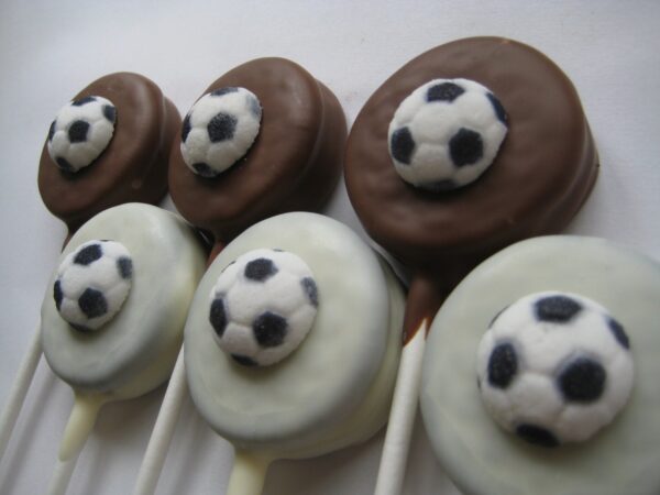Soccer ball-themed Oreo lollipops made of chocolate and white coatings arranged on sticks.