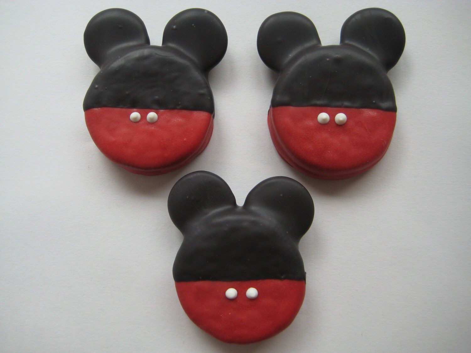 Three Mickey Mouse Chocolate Covered Oreos with black ear shapes and red bottoms, each featuring two white dots.