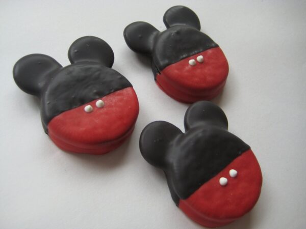 Three Mickey Mouse-shaped Oreos are coated in chocolate with red accents and two small white dots each.