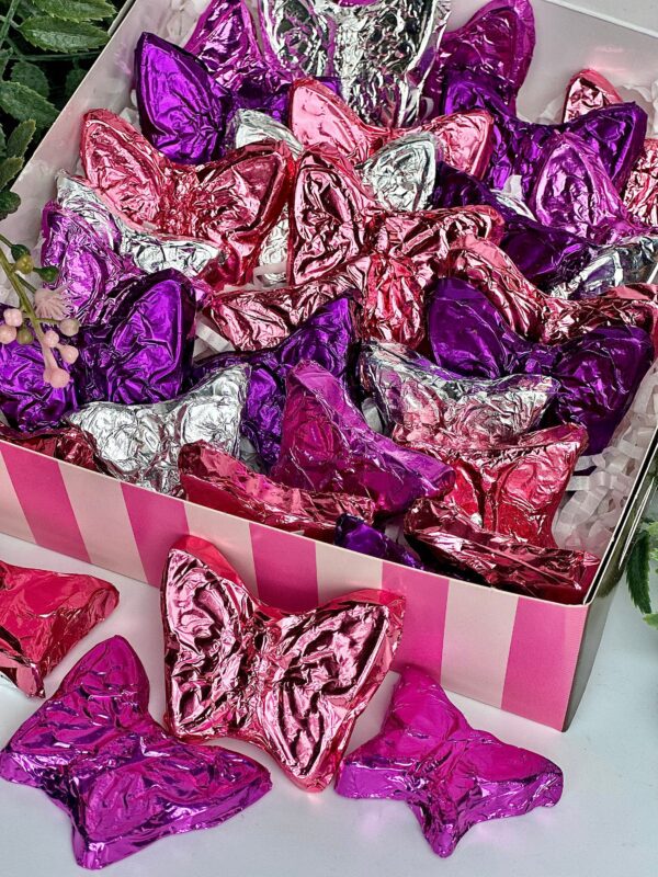 A Foil Wrapped Milk Chocolate Butterflies Gift Box for any occasion includes chocolates in pink, purple, and silver foil, with some outside the box.