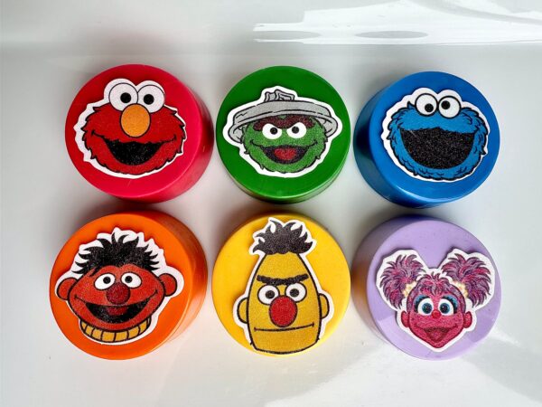 Six colorful Oreo containers, each featuring a Sesame Street character: red with Elmo, green with Oscar, blue with Cookie Monster, orange with Ernie, yellow with Bert, and purple with Abby Cadabby. Perfect for birthdays or monster-themed parties!.