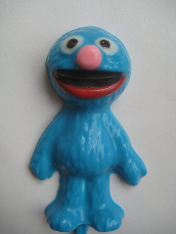 Toy figure resembling a blue, furry character with wide smile, pink nose, and large eyes on solid background is represented in the 12-Grover Chocolate Lollipops For Children’s Party/Birthday Party/Party Favors.