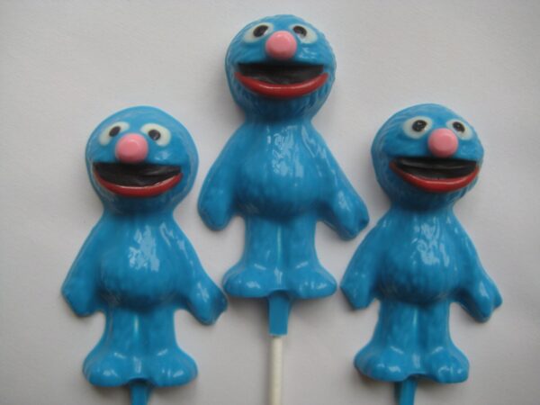 Three Grover-shaped chocolate lollipops with big eyes and wide smiles on sticks.