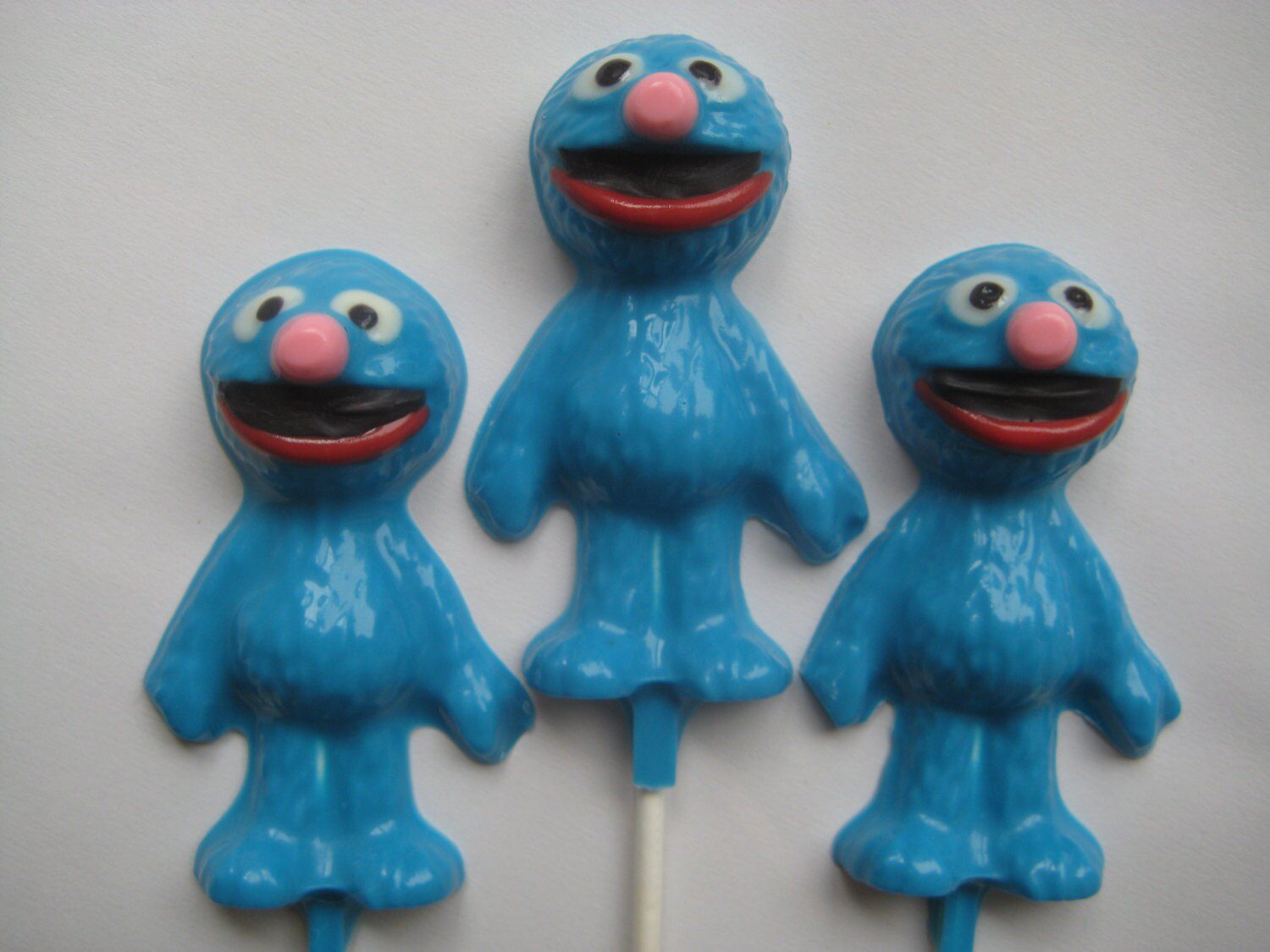 Three Grover-shaped chocolate lollipops with big eyes and wide smiles on sticks.
