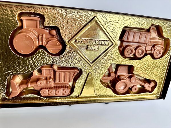 Chocolate gift box featuring construction vehicle shapes like a dump truck and bulldozer, arranged around a "Construction Zone" label.