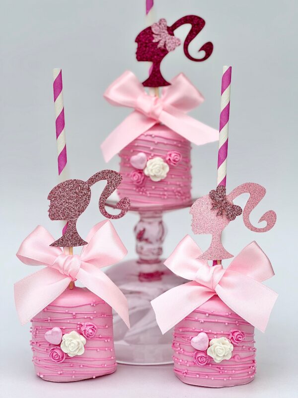 Three pink jumbo marshmallows adorned with glitter silhouette toppers of a woman in ponytails, complete with pink bows and roses.