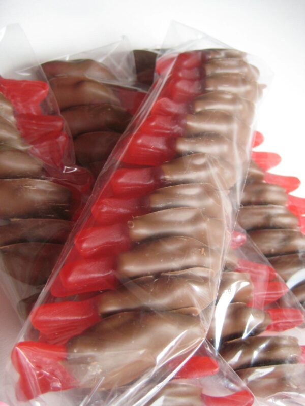 Close-up of chocolate-covered Swedish Fish shaped like cola bottles, wrapped in clear plastic.