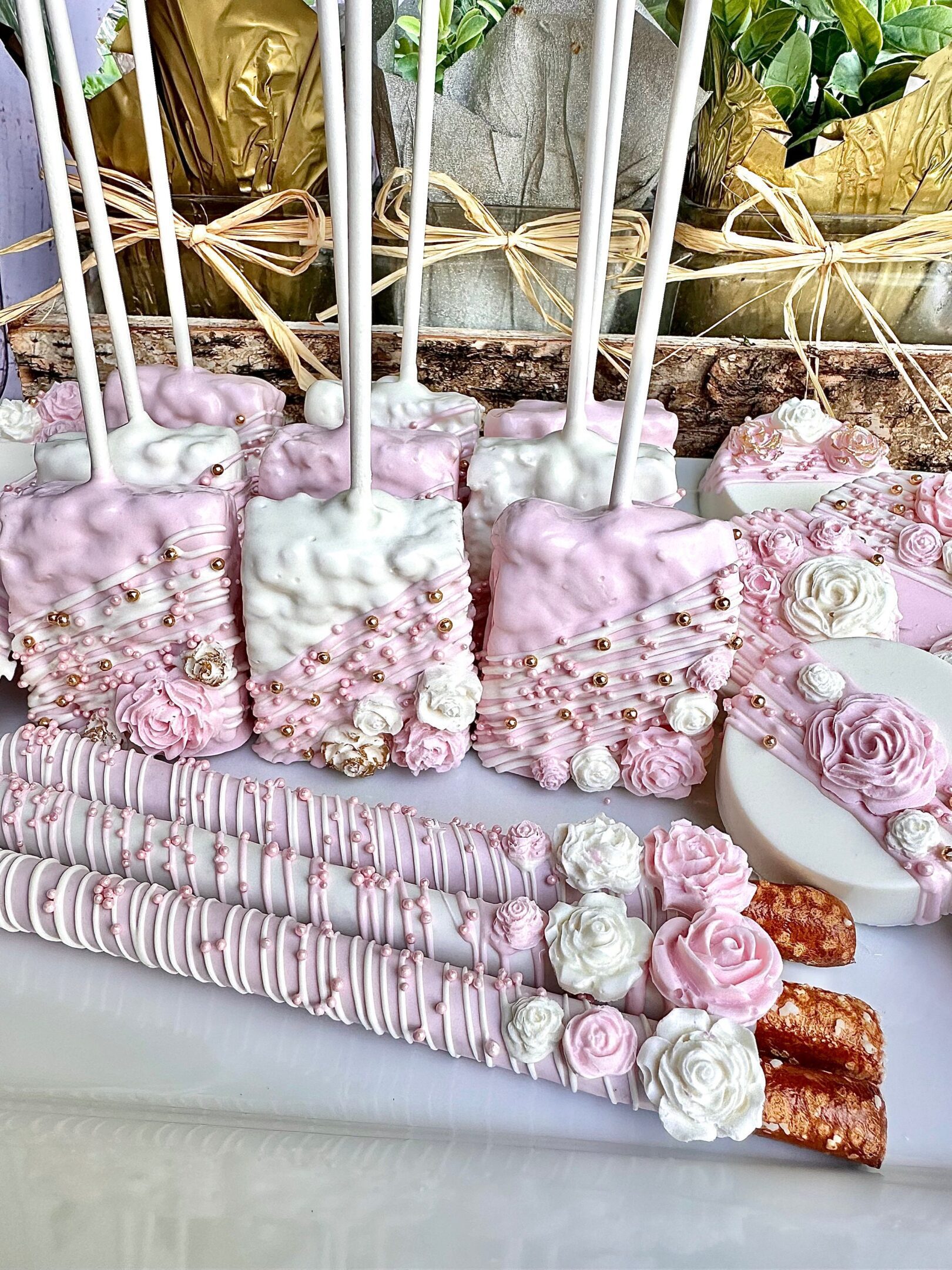 The Pink and White Chocolate Treat Party Bundle for wedding, birthday, or baby shower favors features decorated cake pops, marshmallows, and pretzels displayed on a white surface with roses and pearls.