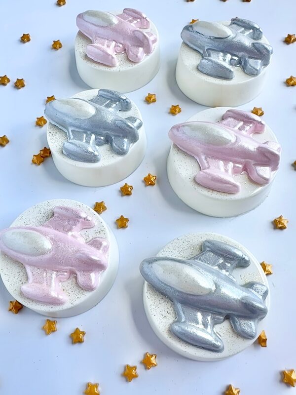 White round soaps feature metallic pink and silver airplane designs with gold star accents, inspired by our 12-Spaceship Chocolate Covered Oreo Favors for a space-themed birthday.