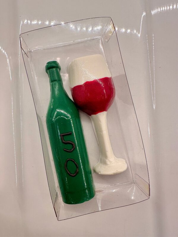 A clear box contains a chocolate crafted into a green wine bottle with "50" and paired with a wine glass, designed for celebrations such as birthdays, anniversaries, or weddings.
