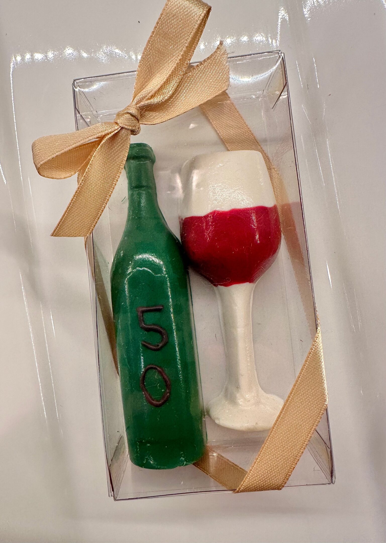 A gift set of 12 chocolate wine glasses and wine bottles in a clear box with a beige ribbon, perfect for birthdays, anniversaries, or weddings.