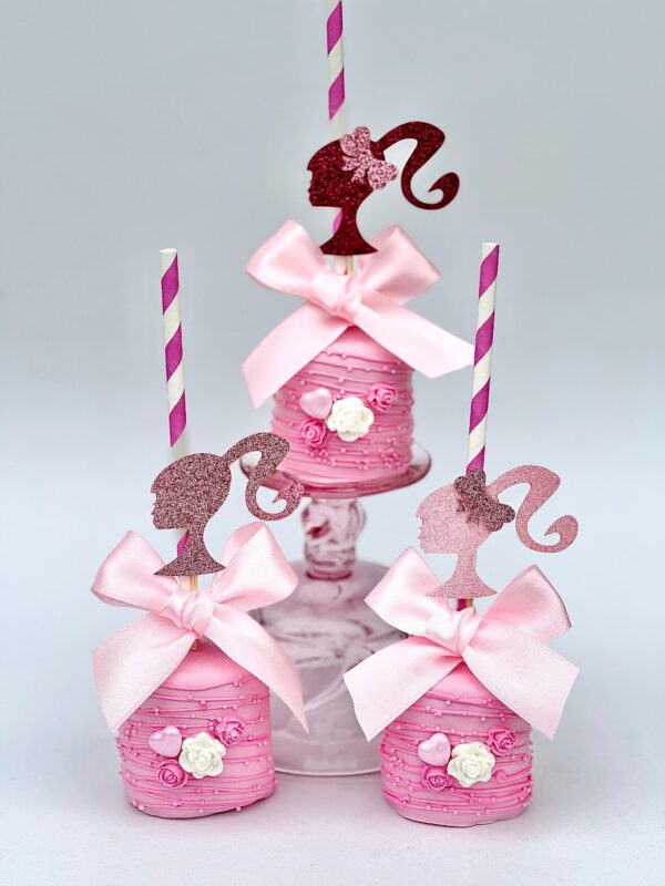 Three chocolate-covered jumbo marshmallows with bows and silhouette toppers, adorned with flowers and arranged on a stand with striped straws.