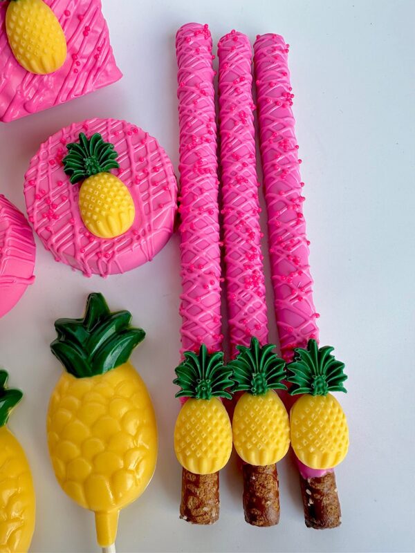 A 48-piece Pink Pineapple Treat Package for birthdays or parties features pink and yellow chocolate-covered pretzel rods and other treats displayed on a white surface.