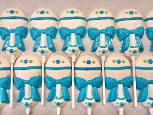 A set of 12-Sweet Baby Boy White Chocolate Baby Rattle Lollipop favors, designed for boys or baby showers, features blue and white rattles with bows and dots.