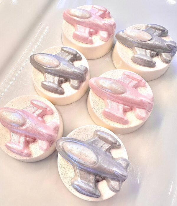 Six of the 12 spaceship-themed chocolate-covered Oreos, decorated with metallic pink and silver airplanes, are displayed on a white surface.