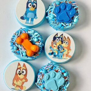 Indulge in 12 chocolate-covered Oreos designed with a "Bluey" theme, showcasing character images, blue paw prints, and orange bone shapes, all enhanced with blue and orange sprinkles. Perfect for birthday party favors!.