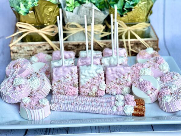 A display of the Pink and White Chocolate Treat Party Bundle for events, featuring pretzel rods, marshmallows, and cookies with floral and bead decorations on a platter.