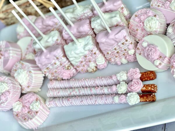 Pink and white decorated desserts including cake pops, pretzel sticks, and round treats with floral and pearl details are featured in the Pink and White Chocolate Treat Party Bundle, perfect for wedding, birthday party favors, or a baby shower.