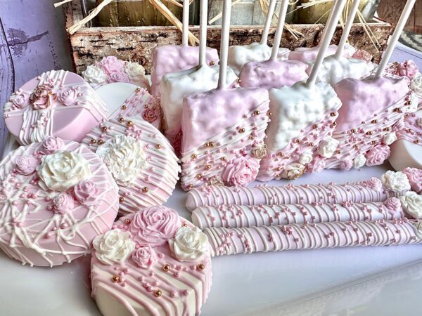 The Pink and White Chocolate Treat Party Bundle features flower and pearl-decorated pink and white desserts like cake pops, cookies, and rice treats, perfect for wedding favors, birthday party favors, or baby shower favors.