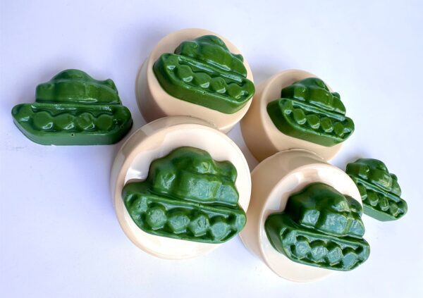 Six chocolates covered Oreos with green, frog-like designs on beige bases, arranged on a white surface.
