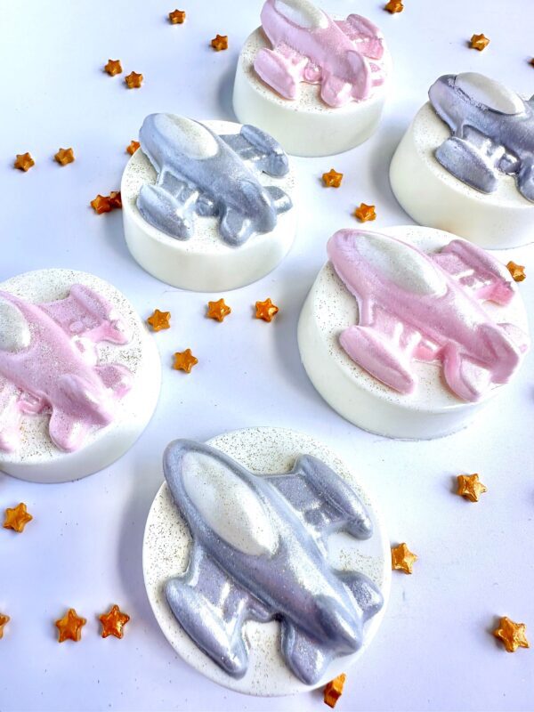 Round soaps featuring silver and pink airplane designs with small gold star decorations on a white background, similar to the 12-Spaceship Chocolate Covered Oreo Favors for birthday parties or space ship themed events.