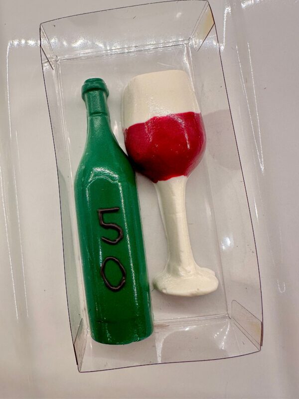 A clear box holds a green chocolate wine bottle with "50" and a red and white wine glass made of cake from the "12-Chocolate Wine Glasses and Wine Bottles" set for celebrations.