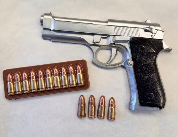 A silver and black chocolate handgun is presented with a row of chocolate bullets, some in a case and others loose, nicely arranged on a plain surface. Perfect as a boxed gift for birthdays, dads, sons, or police officers.