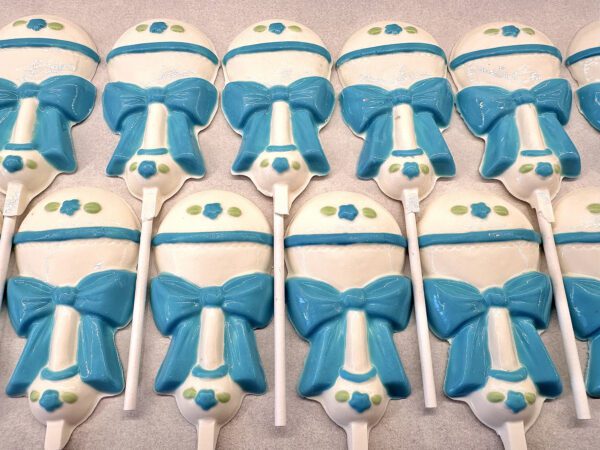 Rows of "12-Sweet Baby Boy White Chocolate Baby Rattle Lollipop Favors" featuring blue bows and decorative accents.