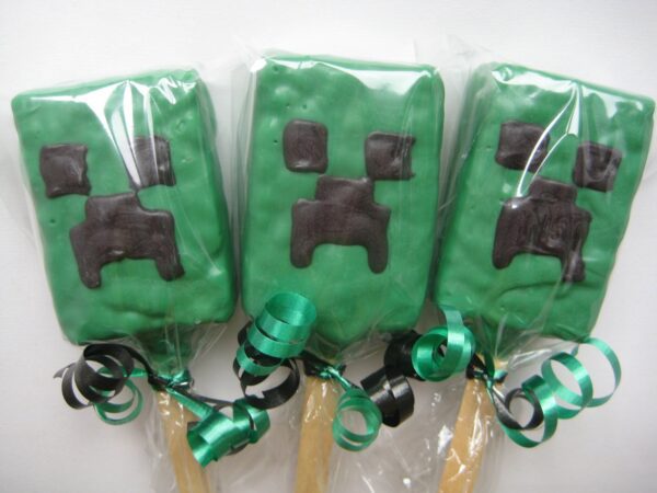 Three Creeper-themed chocolate-covered rice krispie treats with black pixelated faces and green ribbons, wrapped in clear plastic.