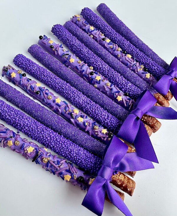 A row of 12-Pretty Purple Pretzels is coated in purple chocolate with sprinkles and decorated with purple bows, perfect for birthday or wedding favors.