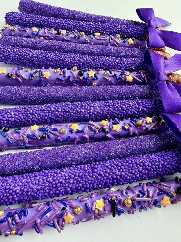 The 12-Pretty Purple Pretzels, designed as party or wedding favors, are chocolate-covered and adorned with sprinkles and bows, arranged in a row.