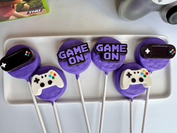 12 'Game On' chocolate-covered Oreo pops with video game controllers, displayed on a white platter.