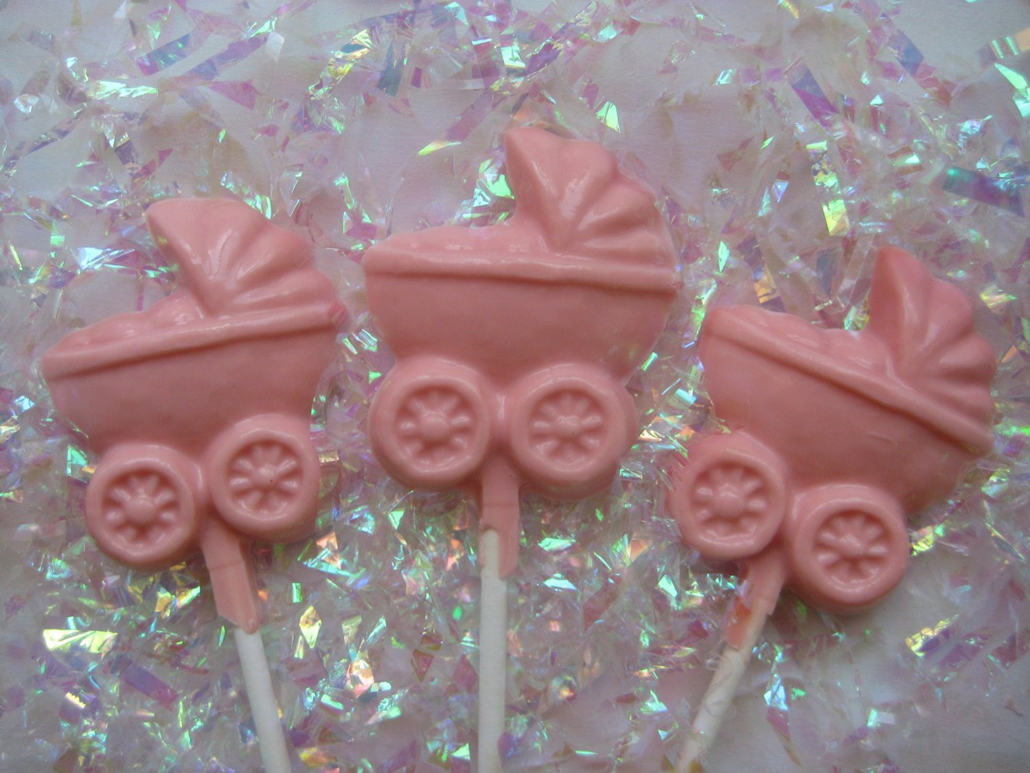 Three chocolate lollipops shaped like baby carriages, perfect for a baby girl shower favor set against a shimmering backdrop.