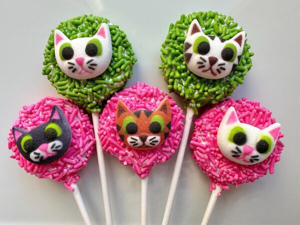 Five 12 Cute Kitty Faces On Chocolate Covered Oreo Pops, adorned with colorful sprinkles: two green and three pink.