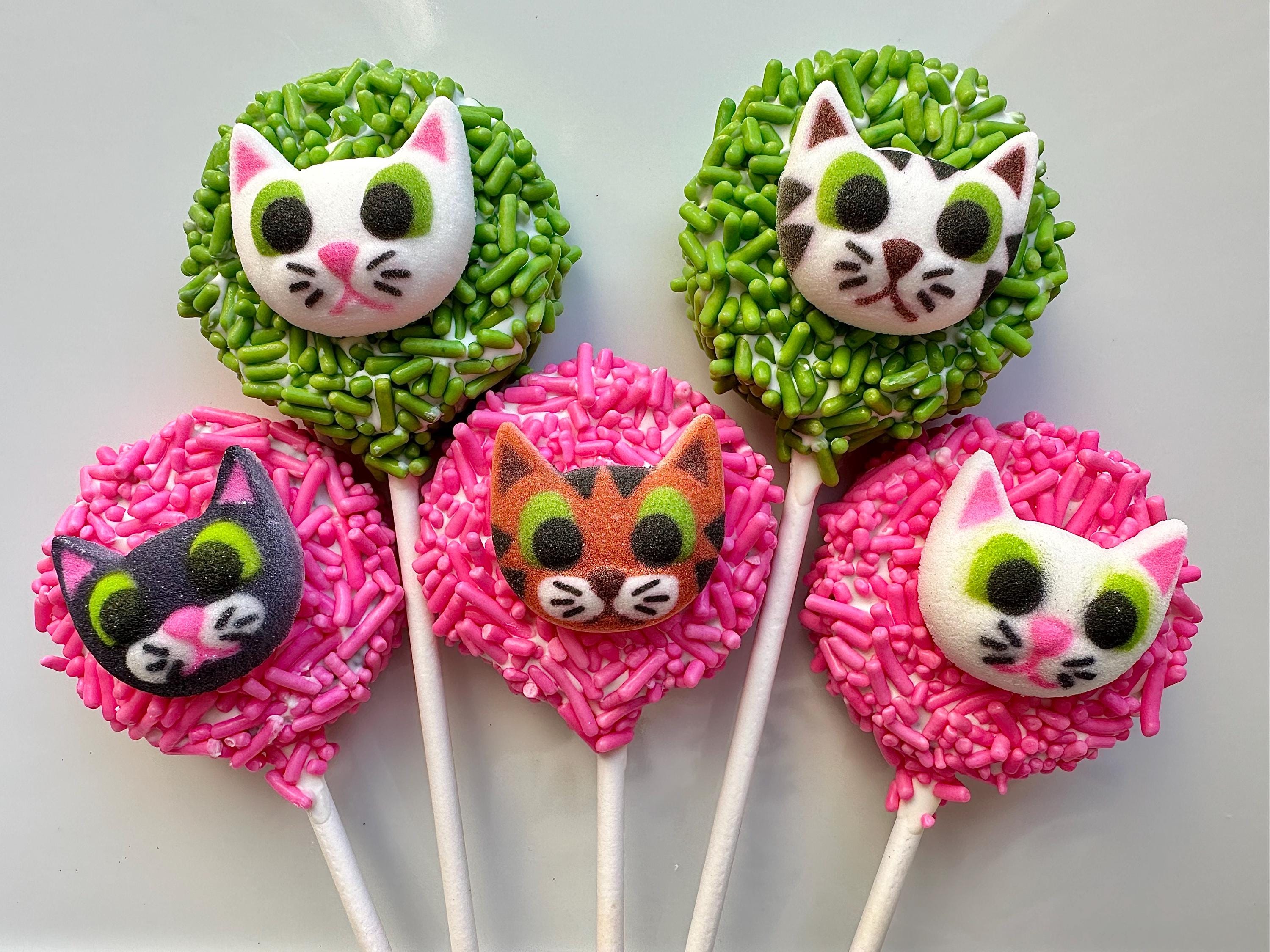 Five 12 Cute Kitty Faces On Chocolate Covered Oreo Pops, adorned with colorful sprinkles: two green and three pink.