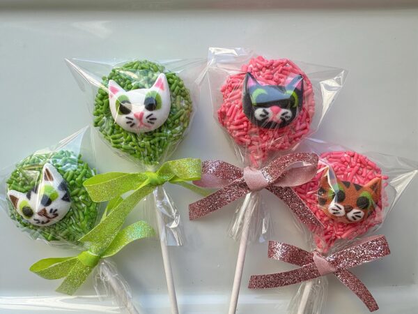 Four Oreo pops, each covered in chocolate and decorated with cute kitty faces, colorful frosting, and sprinkles.