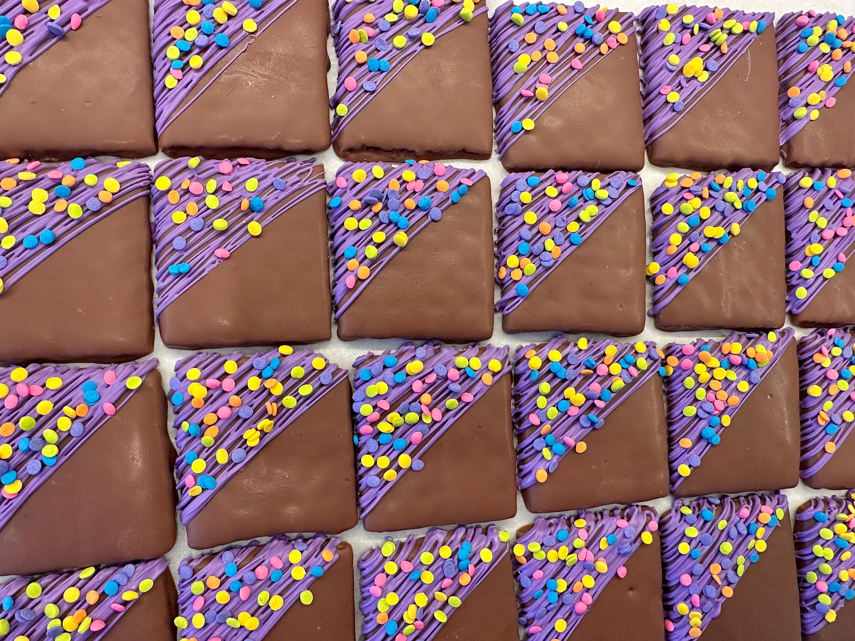 12 Confetti Chocolate Covered Graham Crackers feature a grid pattern of chocolate glaze, purple icing, and colorful sprinkles, perfect for birthdays or party favors.