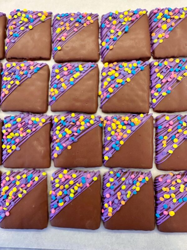 Confetti chocolate-covered graham crackers with purple icing and colorful sprinkles, arranged in a grid pattern.